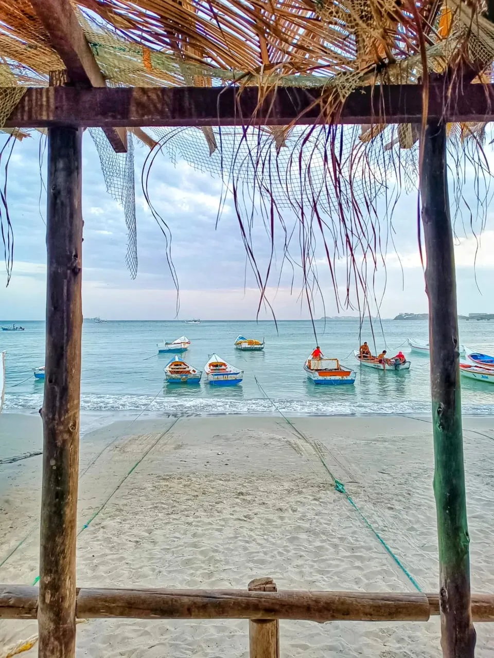 Encantadora playa de la Isla de Margarita con botes coloridos y vista desde una palapa.